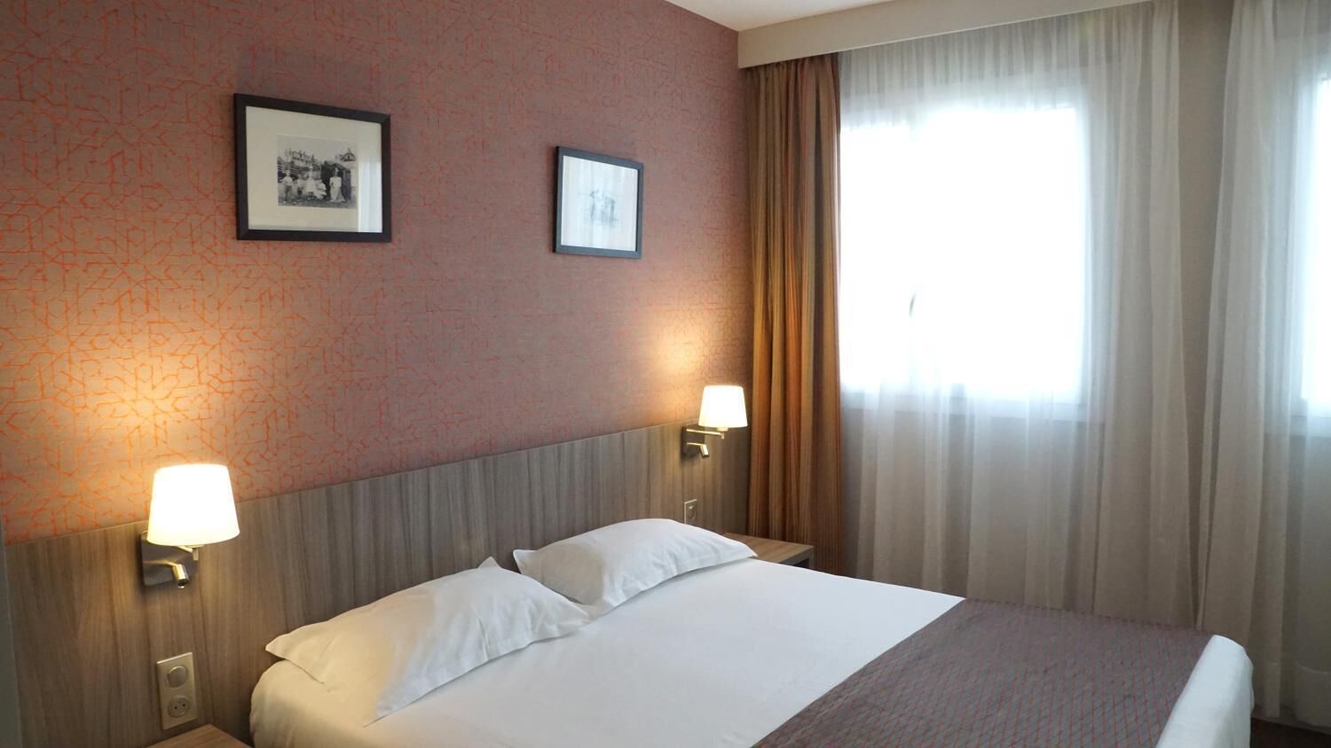 Una habitación de hotel con una cama, dos lámparas de pared y dos cuadros colgados.
