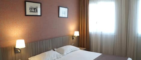 Una habitación de hotel con una cama, dos lámparas de pared y dos cuadros colgados.