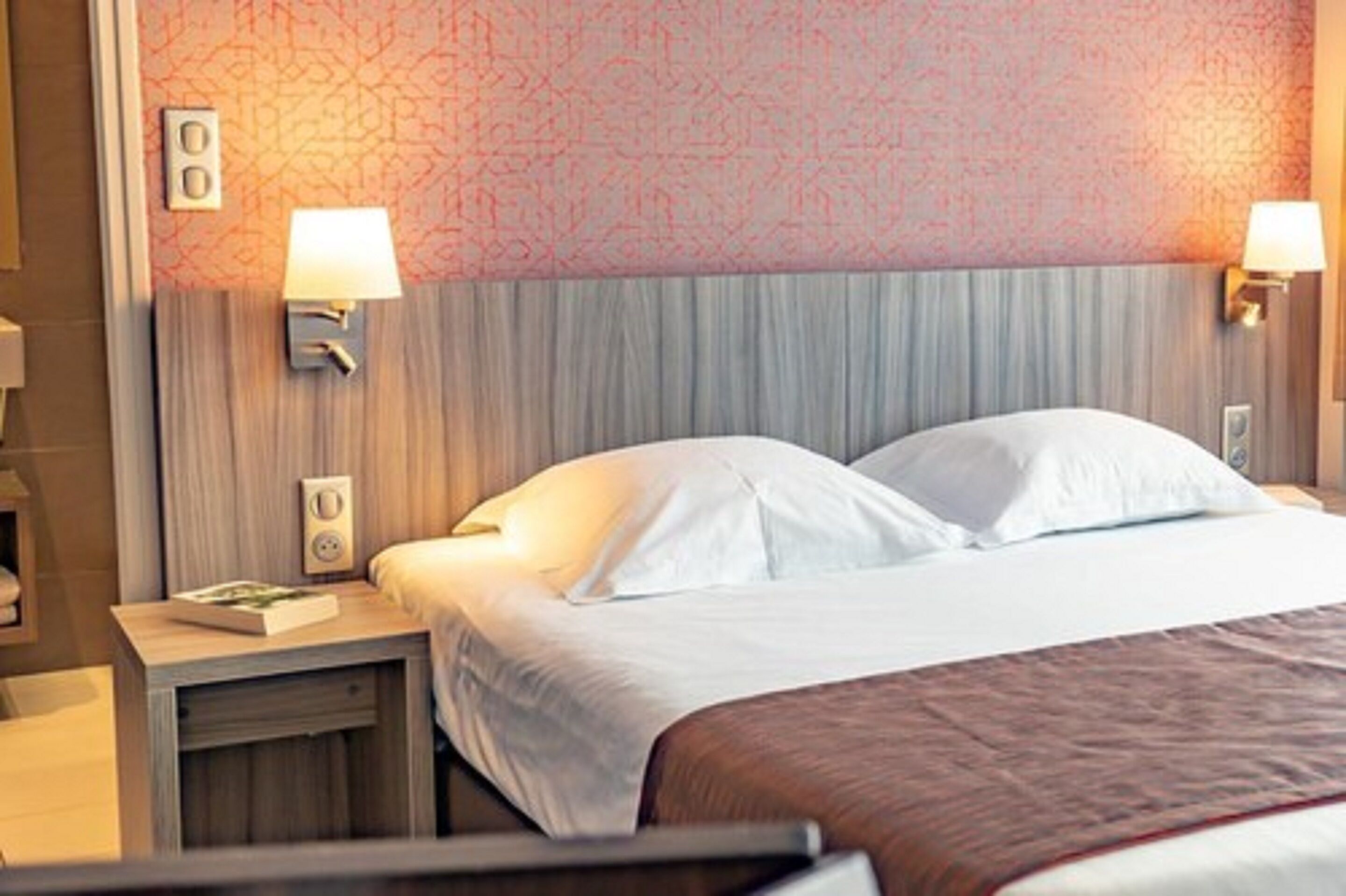 Una camera d'albergo con un letto, comodini e lampade a parete.