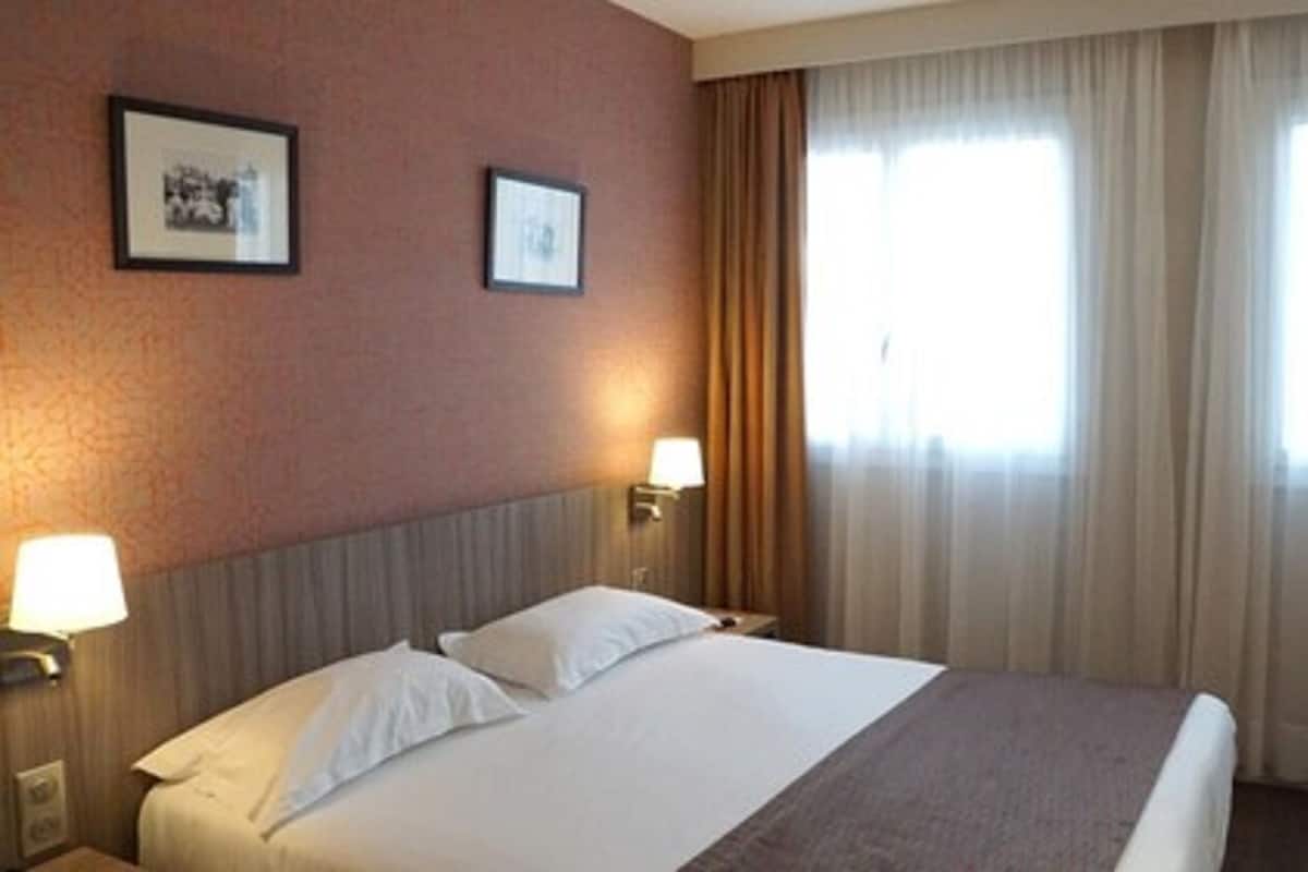 A hotel room with a bed, two wall-mounted lamps, and a window with curtains.
