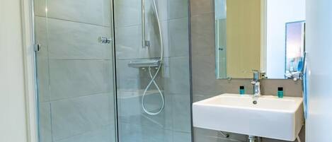 Un baño moderno con ducha de vidrio, lavamanos blanco y tocador de madera.