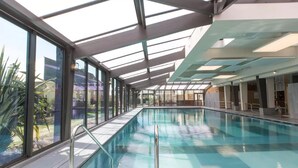 A large indoor swimming pool with glass walls and a skylight, surrounded by a modern architectural design. - Résidence Neptunia (Saint-Malo)
