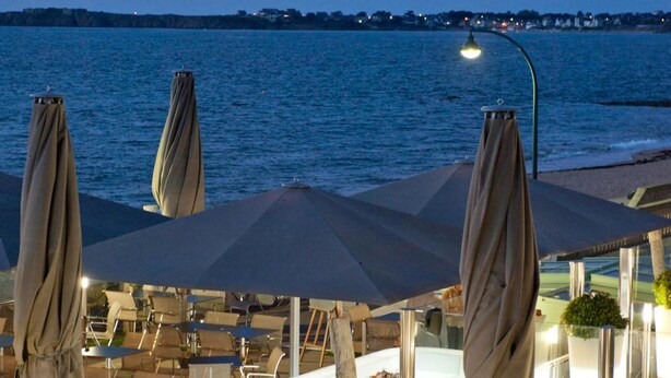 An outdoor dining area with tables and umbrellas overlooking a body of water. - Résidence Neptunia (Saint-Malo)