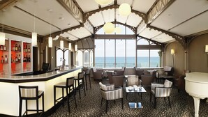 A bar area with a view of the sea, furnished with chairs and tables, and a piano in the corner. - Résidence Neptunia (Saint-Malo)