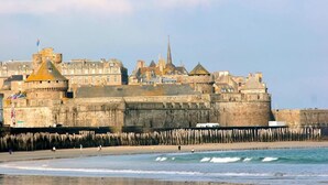 A historic stone castle with multiple towers and a fortified wall, overlooking a beach with waves. - Résidence Neptunia (Saint-Malo)