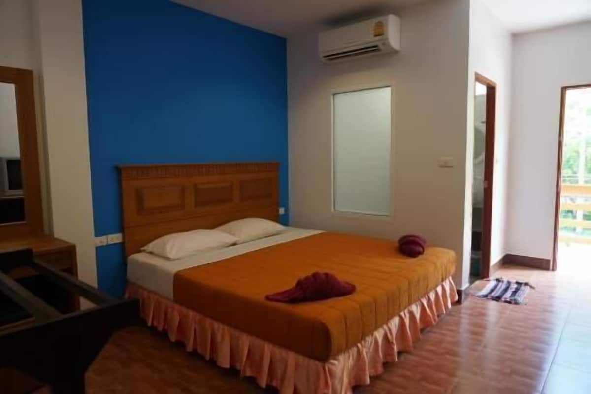 A bedroom with a wooden headboard, a large bed with an orange bedspread, a single window, and an air conditioning unit.