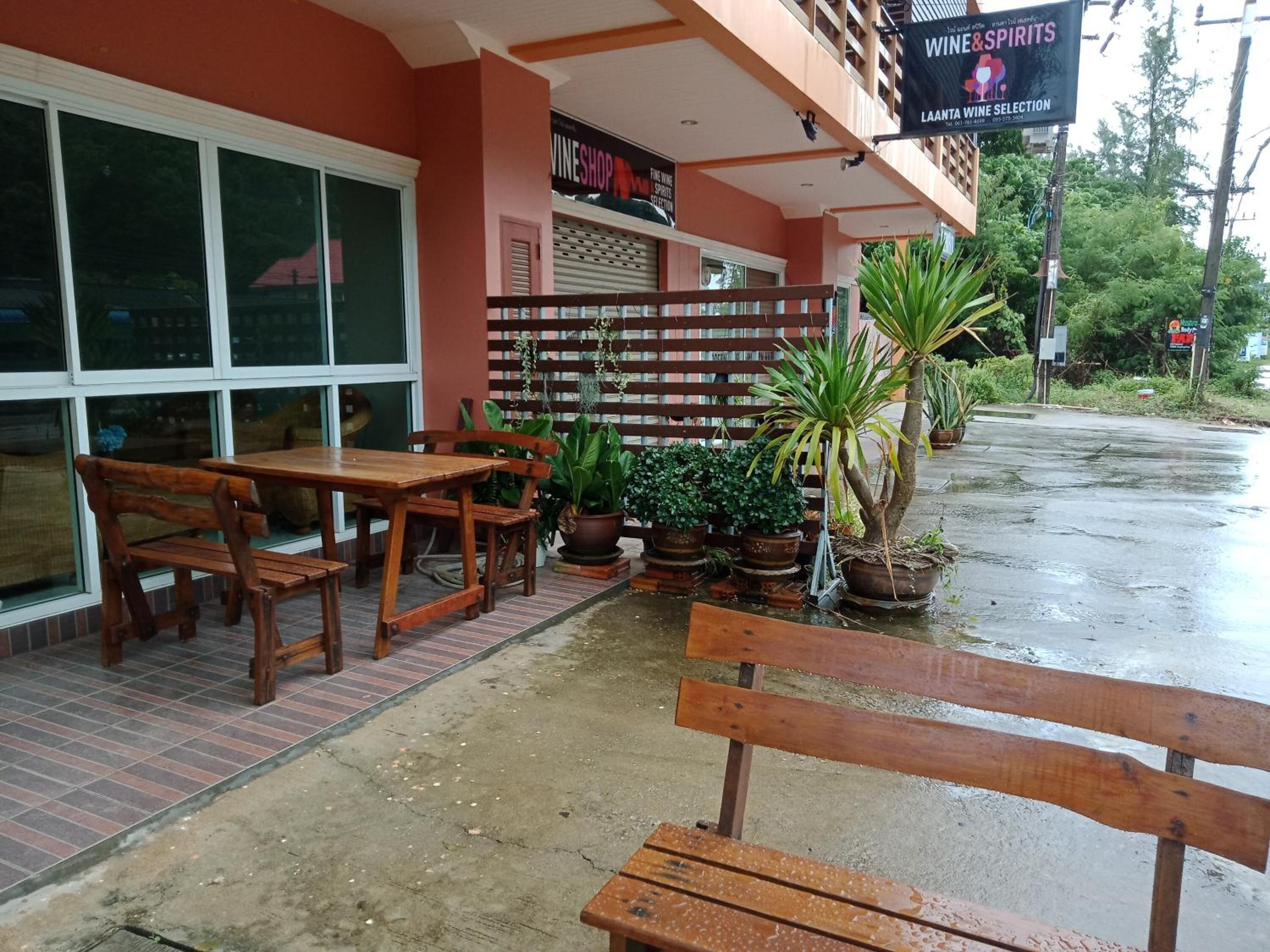 A restaurant with outdoor seating, a wine selection sign, and potted plants.