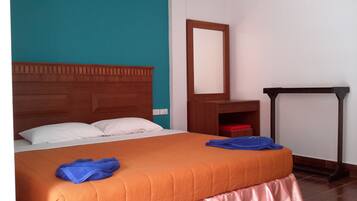 Habitación de hotel con cabecera de madera, cama con colcha naranja, dos almohadas blancas, toalla azul, mesita de noche de madera, espejo y una silla roja.