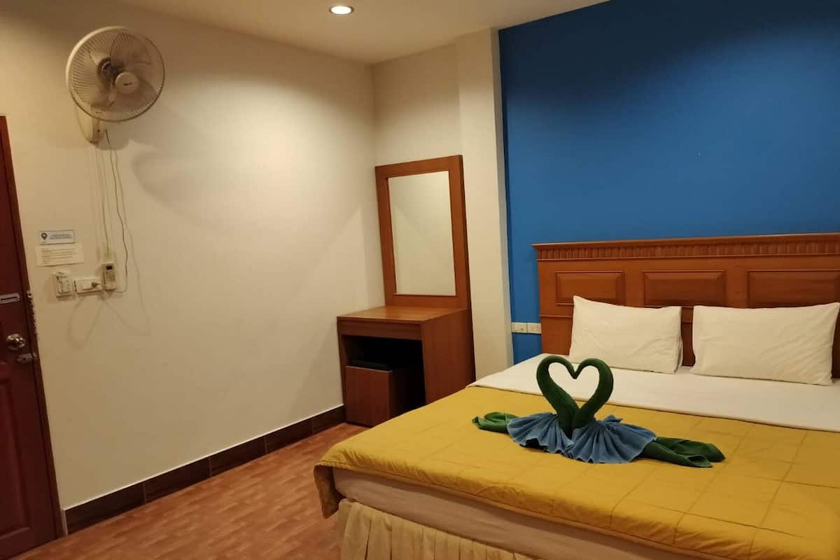 A hotel room with a bed, a wooden nightstand, a mirror, and a wall-mounted fan.