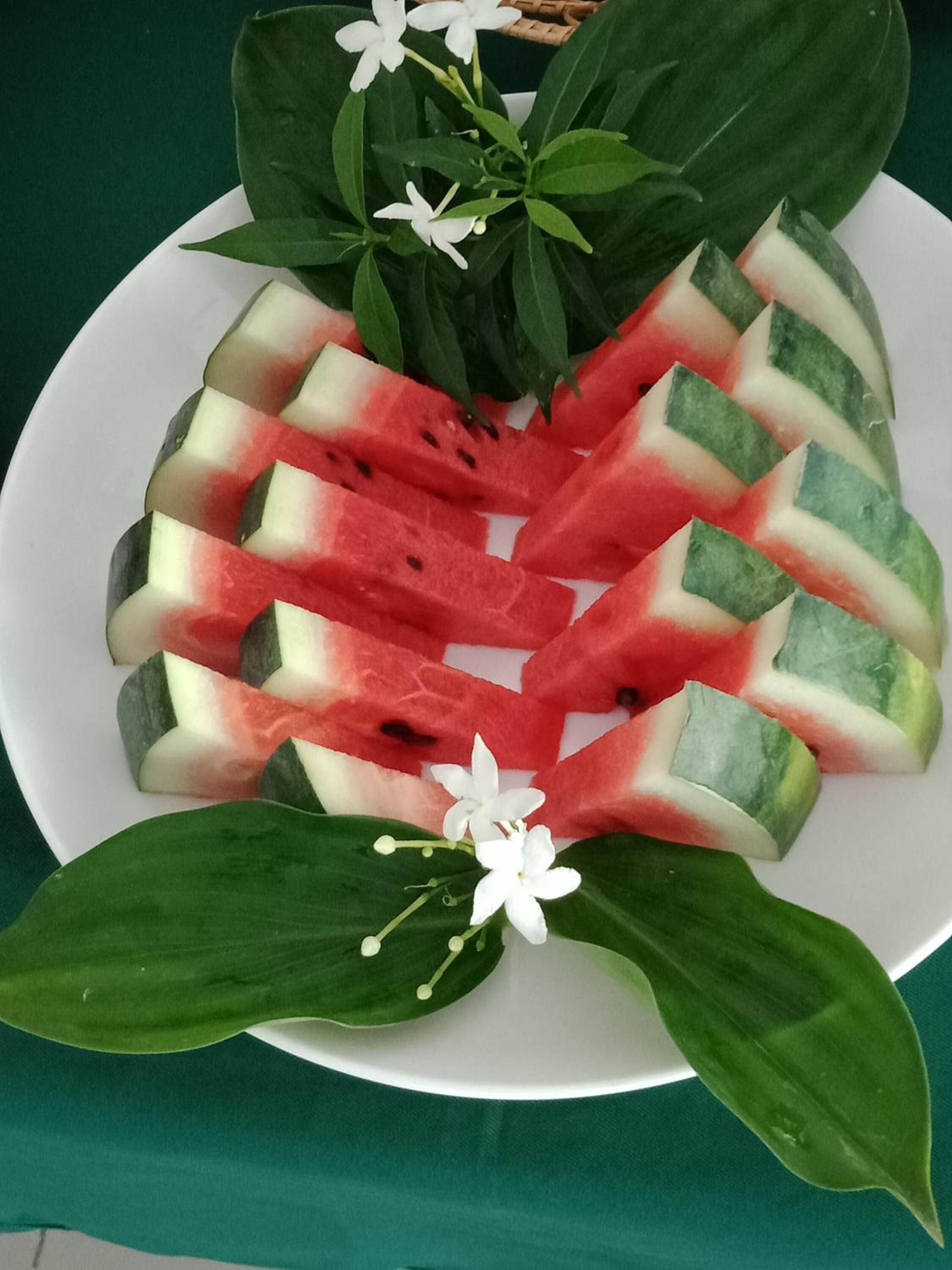 A plate of watermelon slices arranged in a pattern, with green leaves and white flowers on a white plate.
