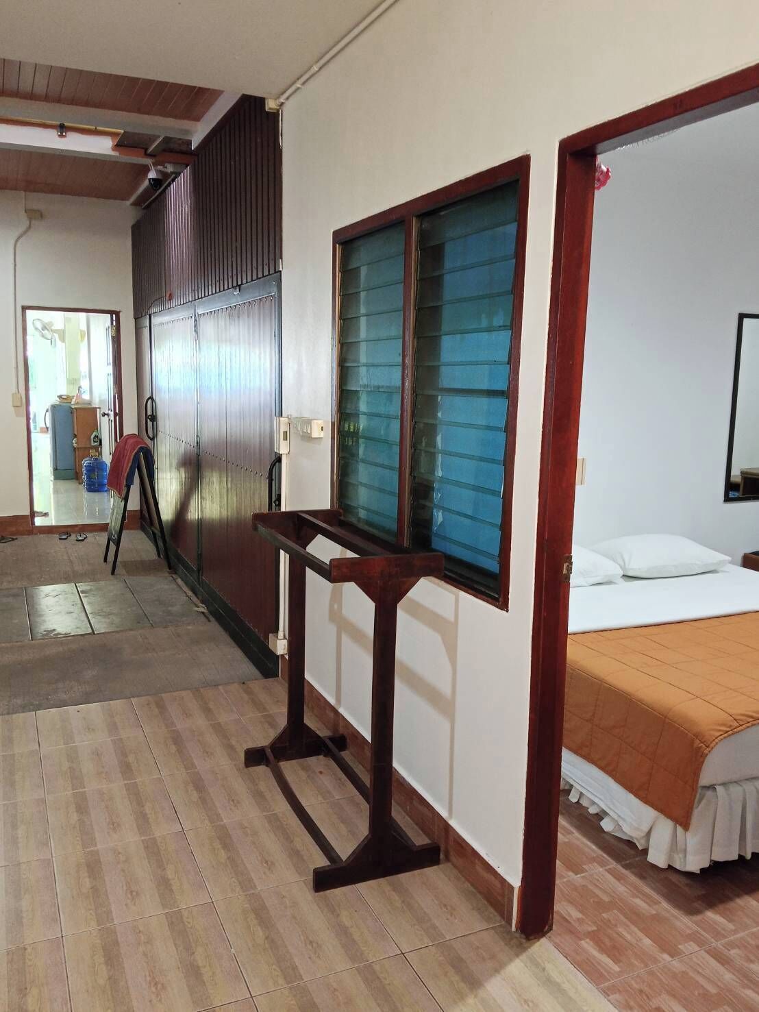 Una habitación con una cama, una ventana con persianas, una mesa de madera y una puerta que da a otra habitación.