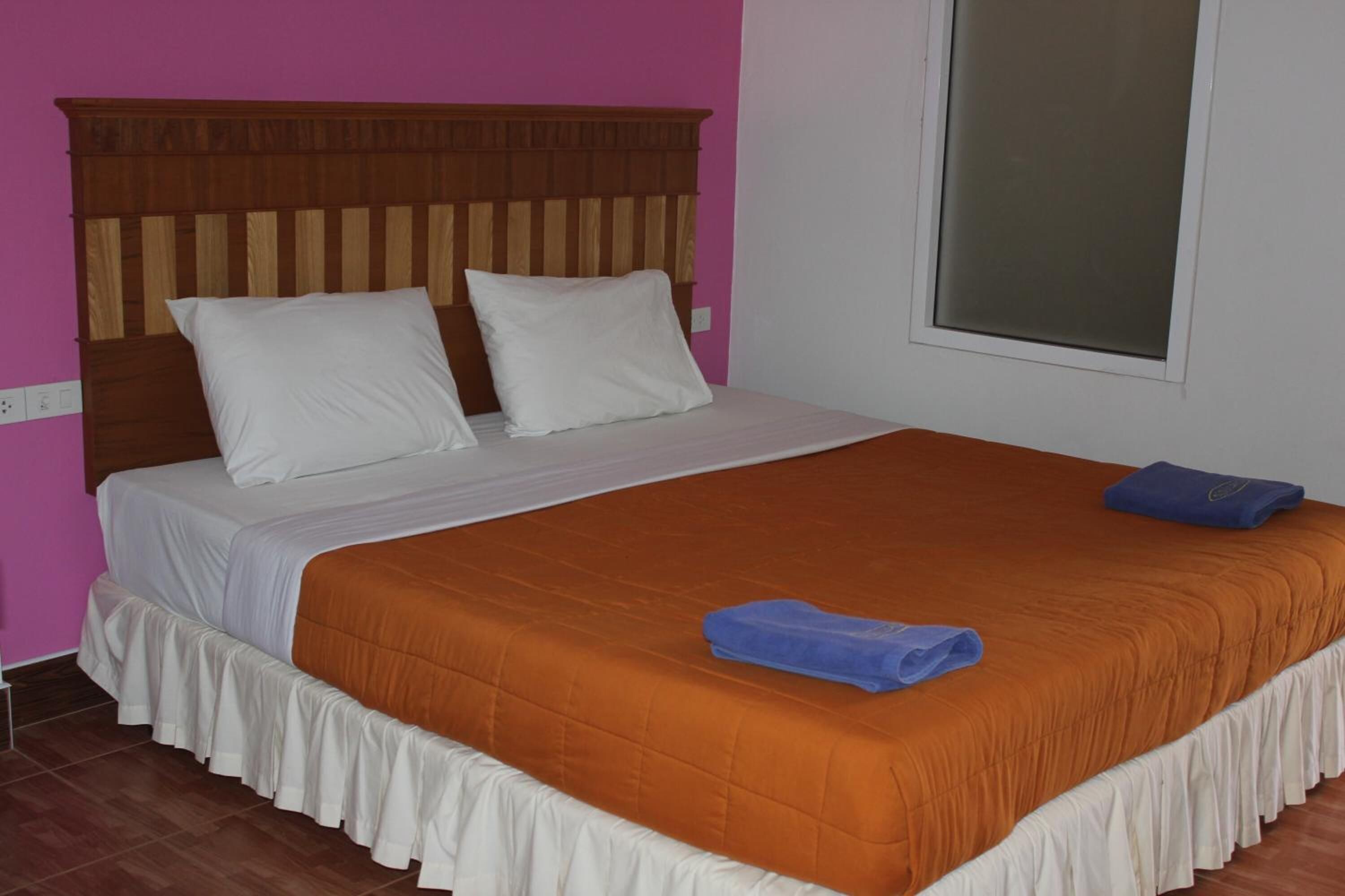 A bed with a wooden headboard, white bedding, and an orange bedspread.