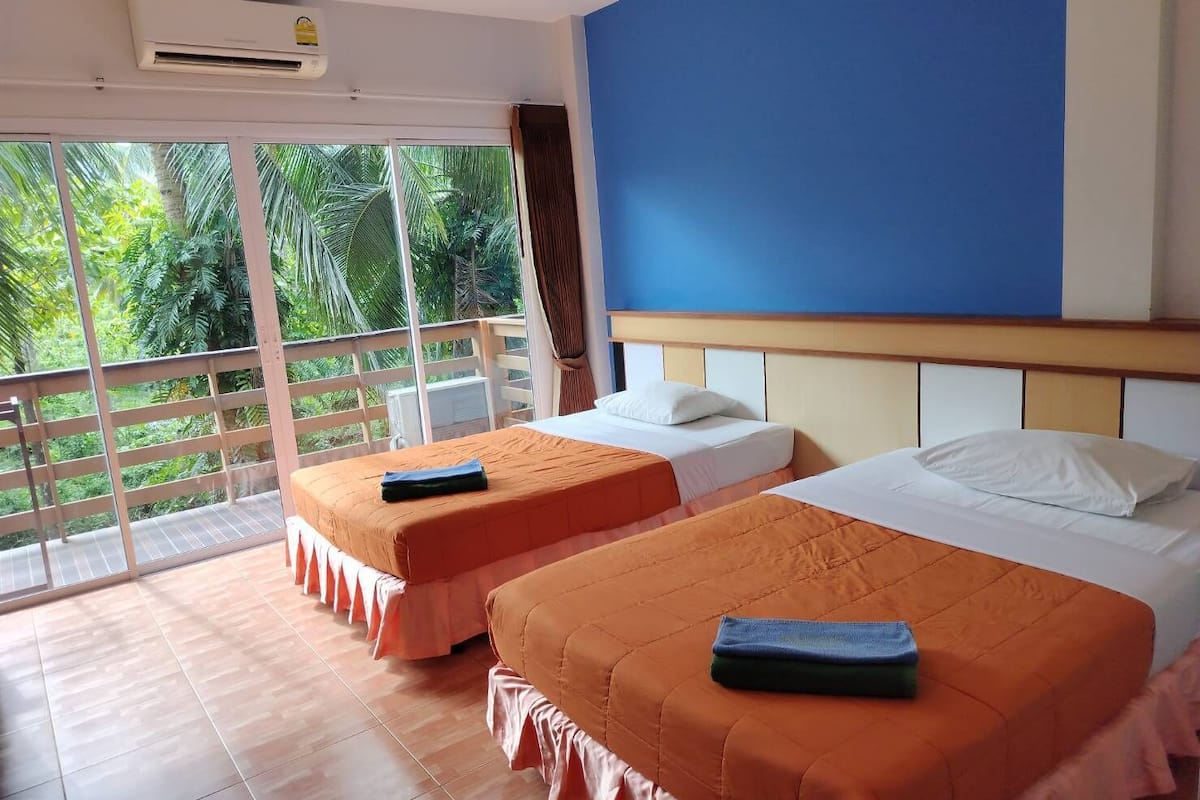 A hotel room with two beds, a balcony, and a view of greenery.