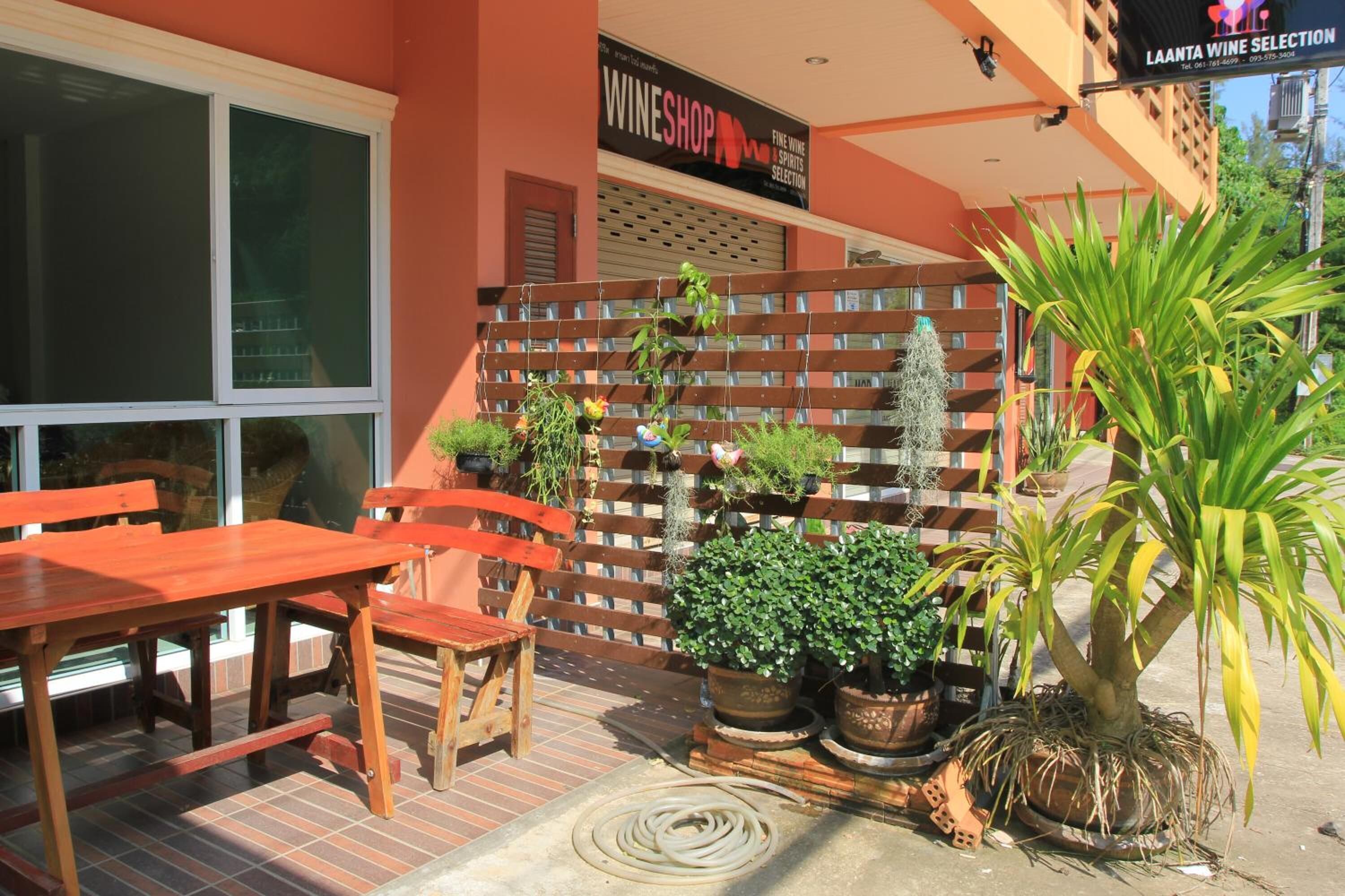 Un espacio al aire libre con mesas y sillas de madera, rodeado de macetas con plantas y una valla de madera.