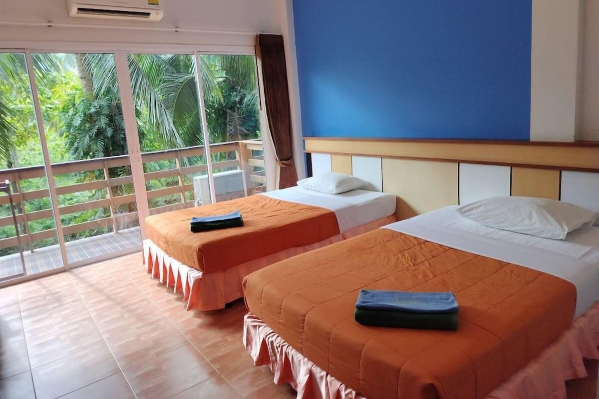 A hotel room with two beds, a balcony, and a view of greenery.