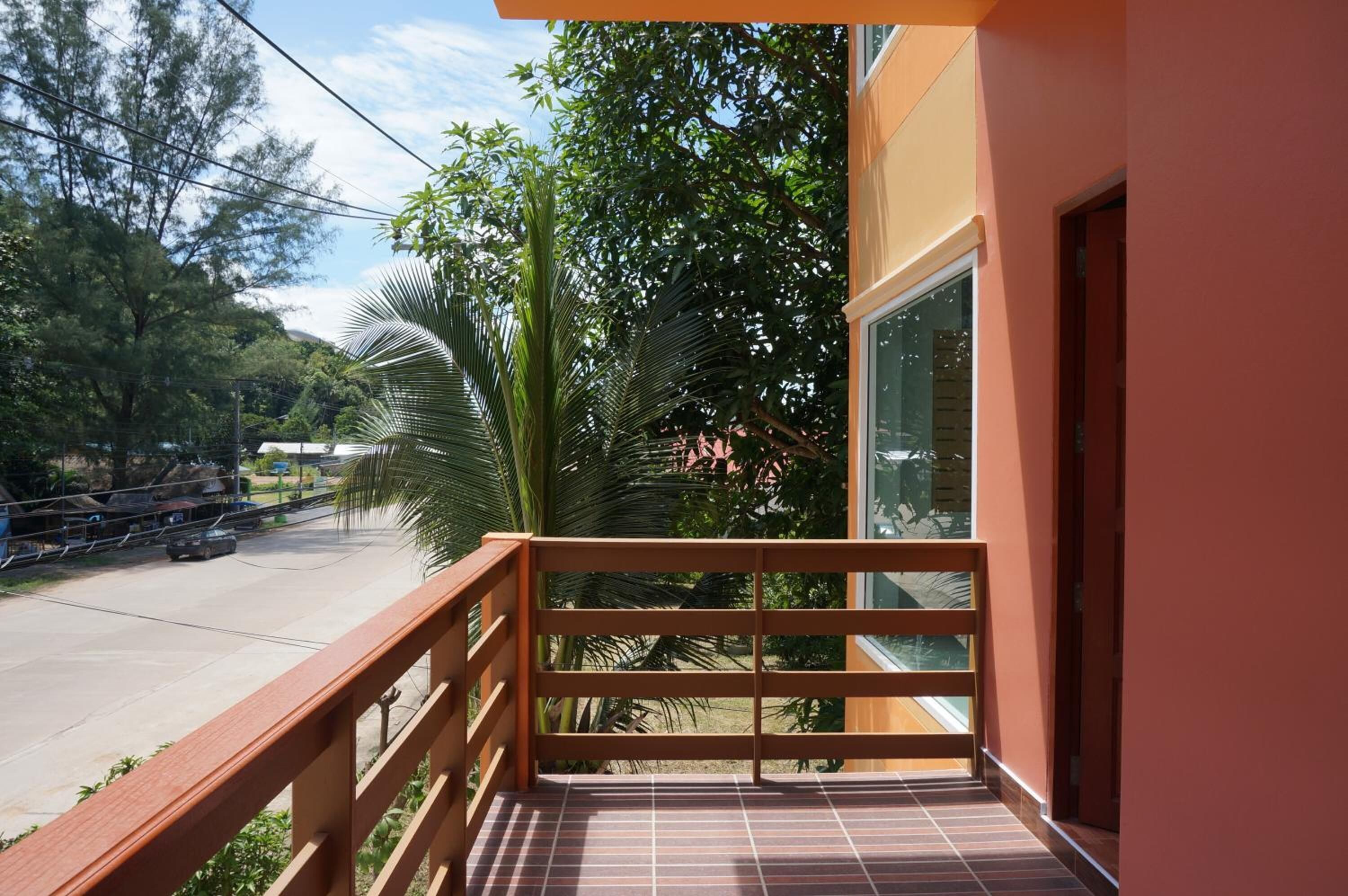 Un balcón con barandilla de madera, suelo de baldosas y vistas a una carretera y árboles.