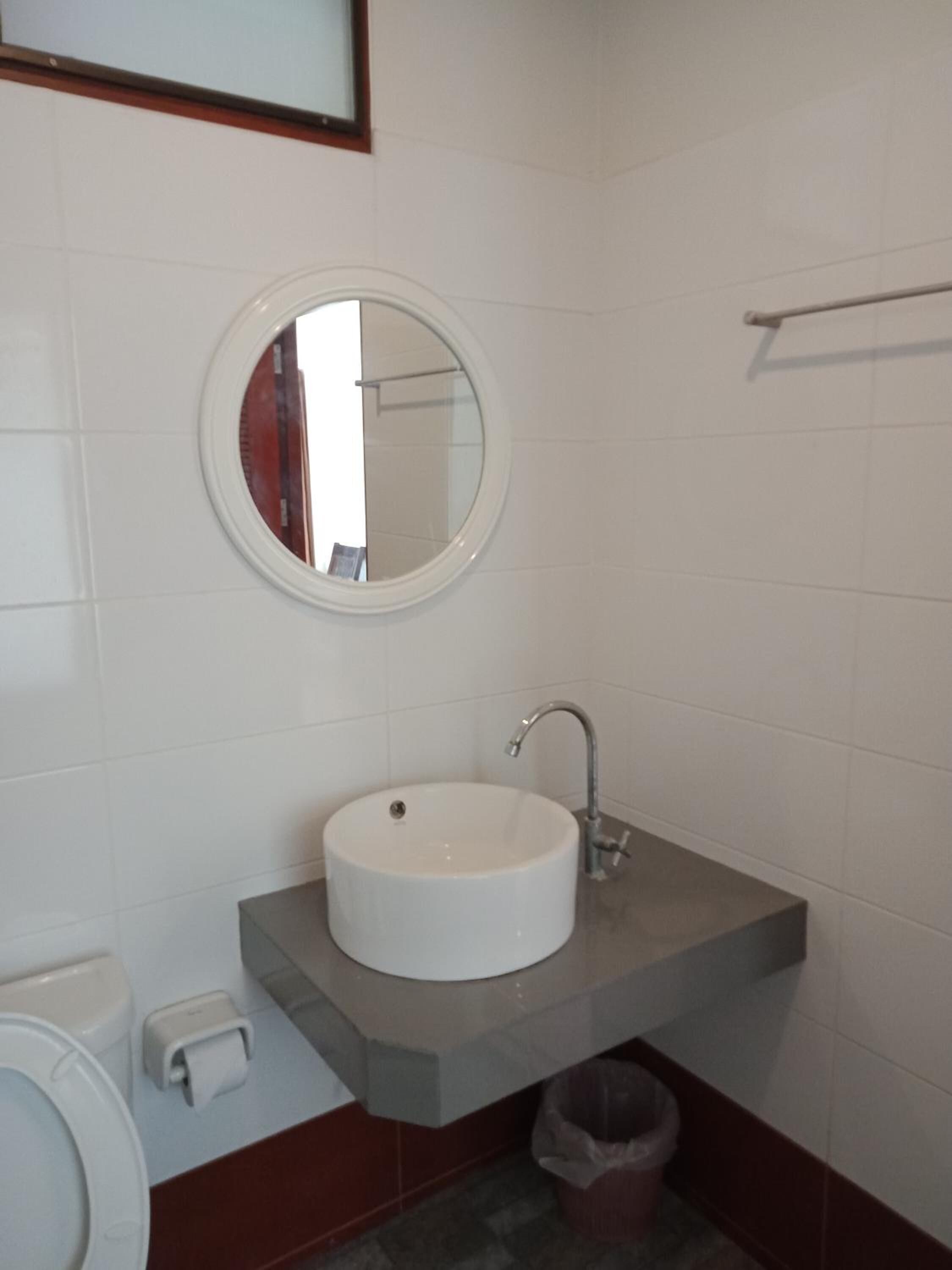 Ein Badezimmer mit einem runden Spiegel, einem Waschbecken und einer Toilette.