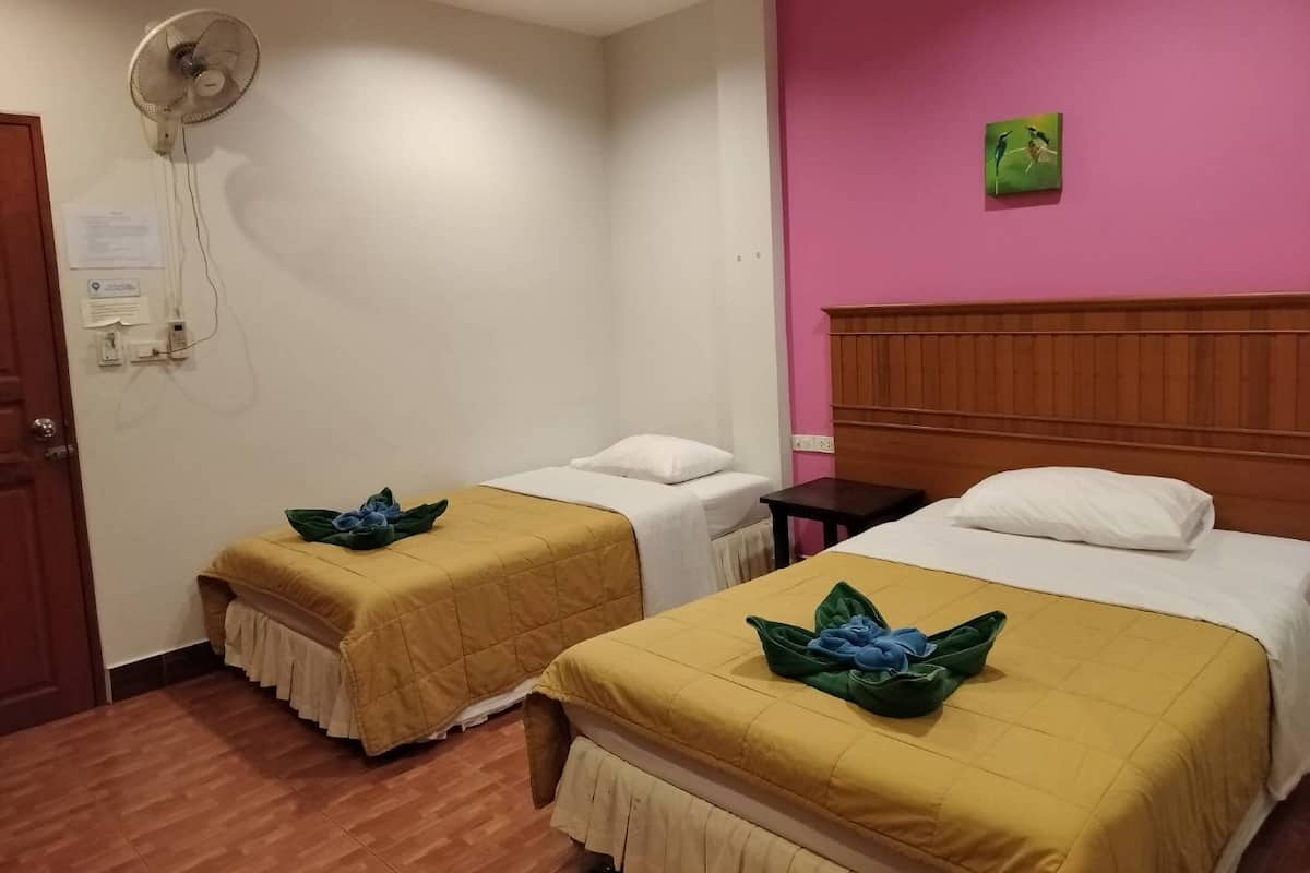 A hotel room with two beds, each with a yellow bedspread and a decorative pillow. There is a wooden headboard on one bed, a small table, and a wall-mounted fan.