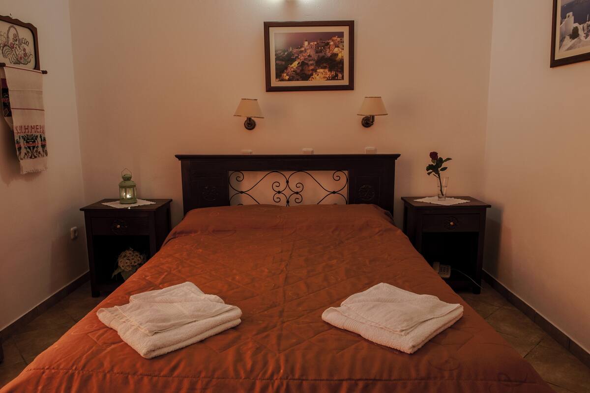 A hotel room with a large bed, two bedside tables, a headboard, a wall-mounted picture, and a wall-mounted lamp.
