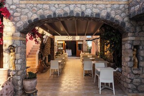 Un espace extérieur aménagé pour les repas, avec des murs en pierre, des meubles en osier blanc et des plantes en pot.