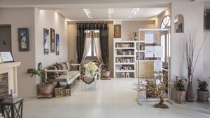 A spacious living room with a fireplace, a bookshelf, and a dining area. - Polydefkis Apartments (Santorini)