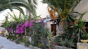 A pathway lined with potted plants and flowers, leading to a building with a stone facade and a wooden door. - Polydefkis Apartments (Santorini)