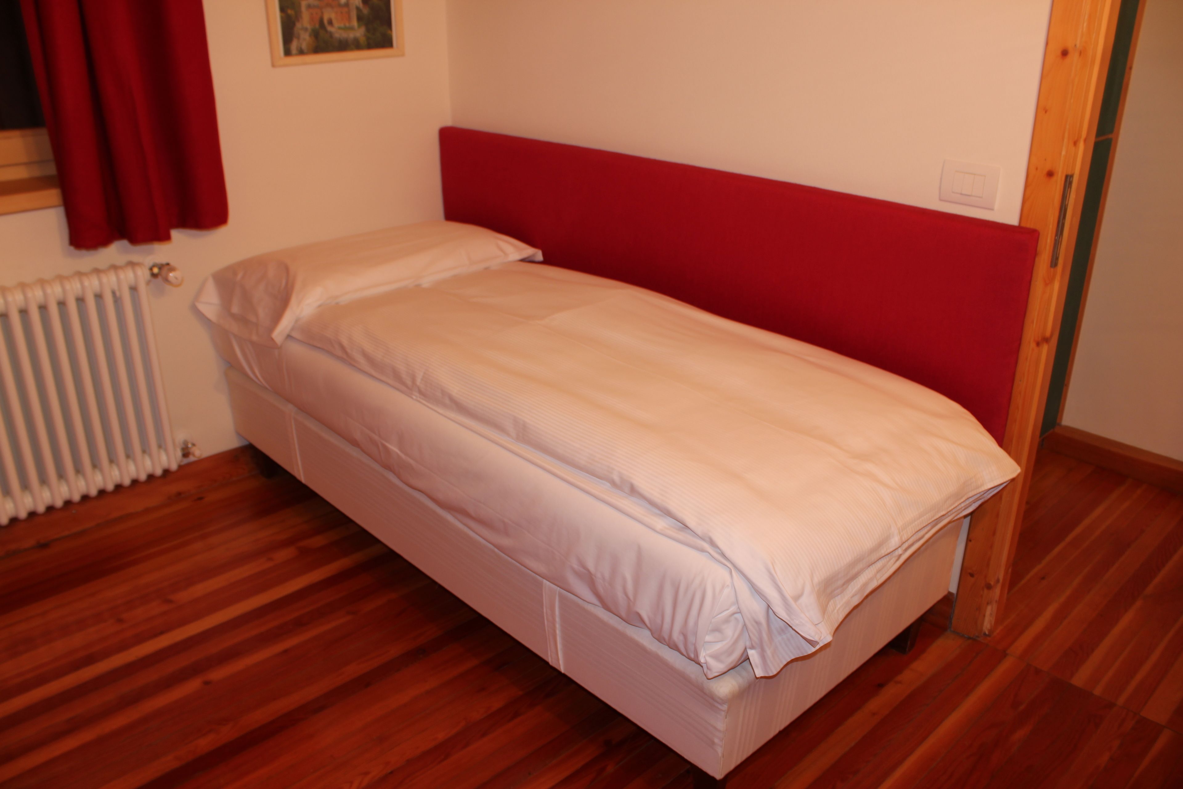 A single bed with a red headboard in a room with wooden flooring and a white radiator.