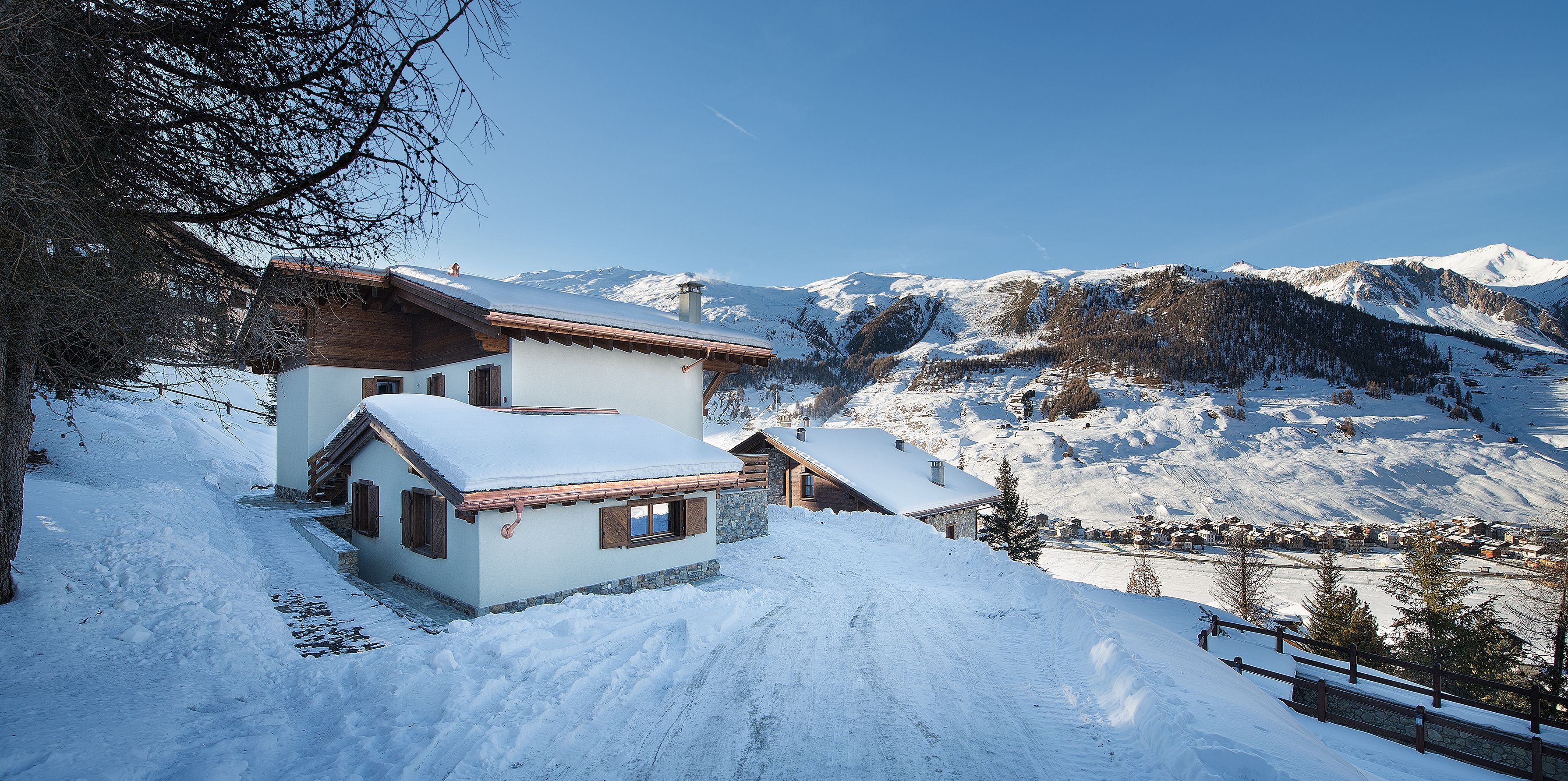 Un villaggio montano innevato con case in legno tradizionali, cielo sereno e vista sulle montagne innevate.