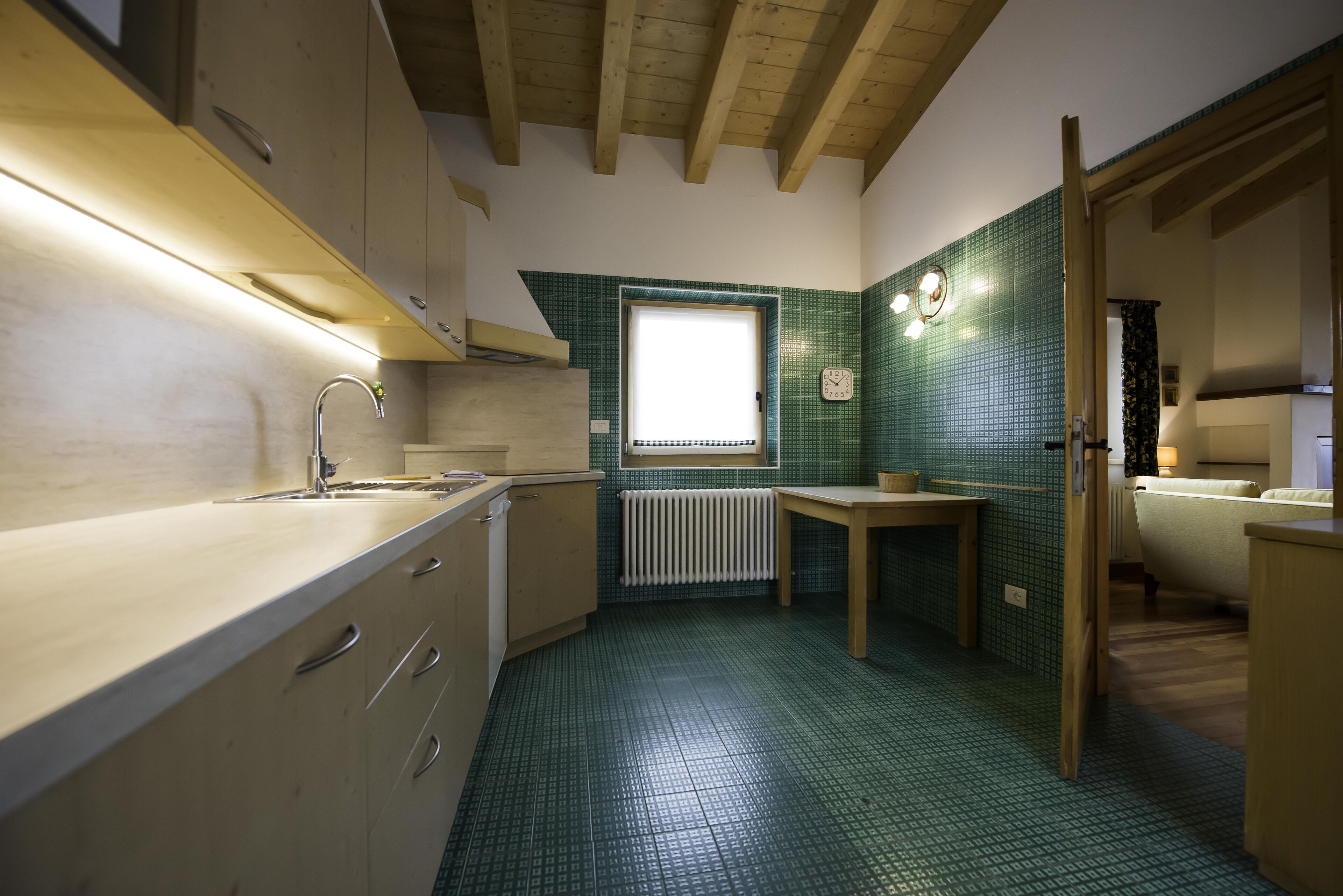 Una cocina pequeña con armarios de madera, un lavamanos, una ventana y piso de baldosas.