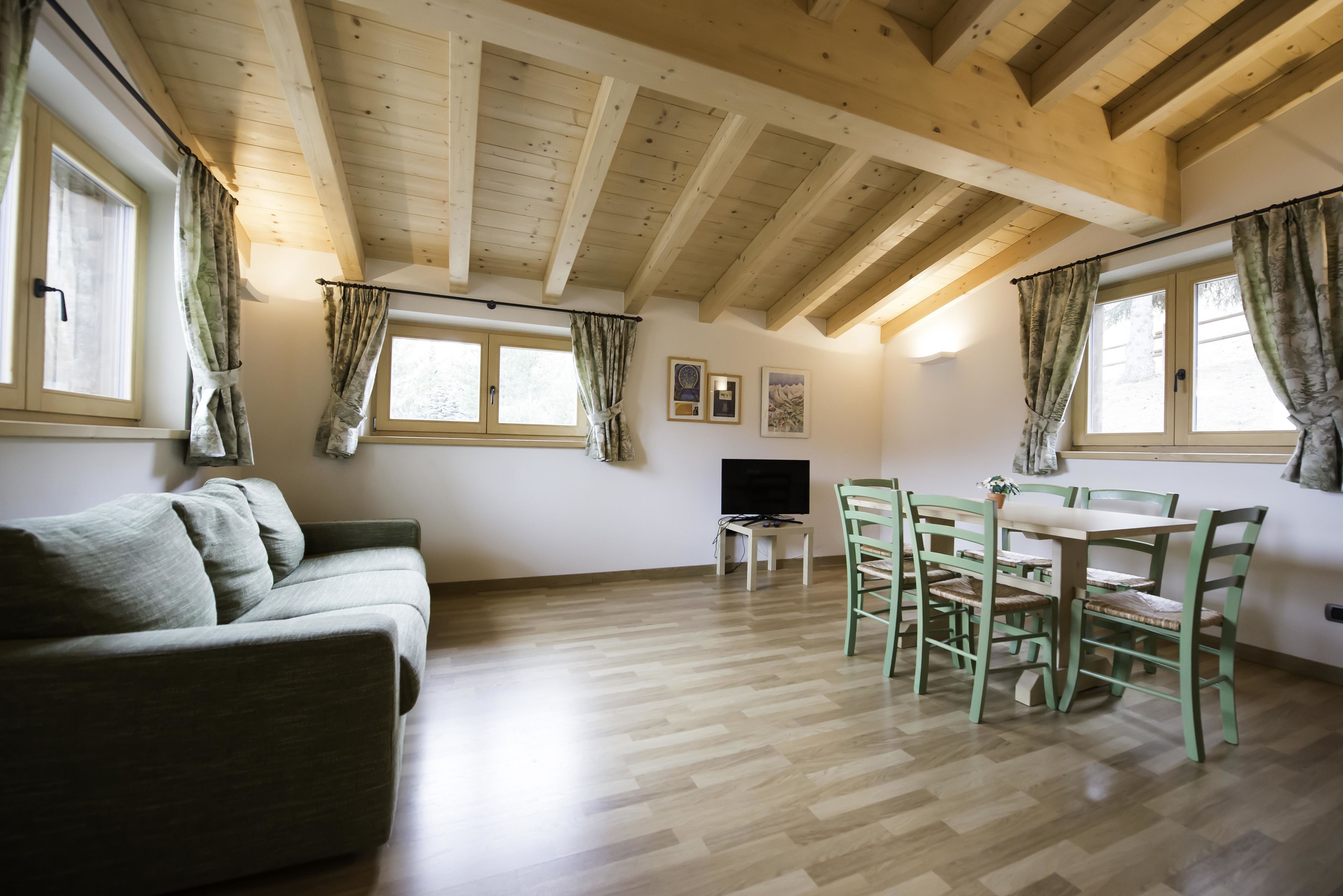 Ein Zimmer mit Holzboden, einer Couch, einem Esstisch mit Stühlen und einem Fernseher.