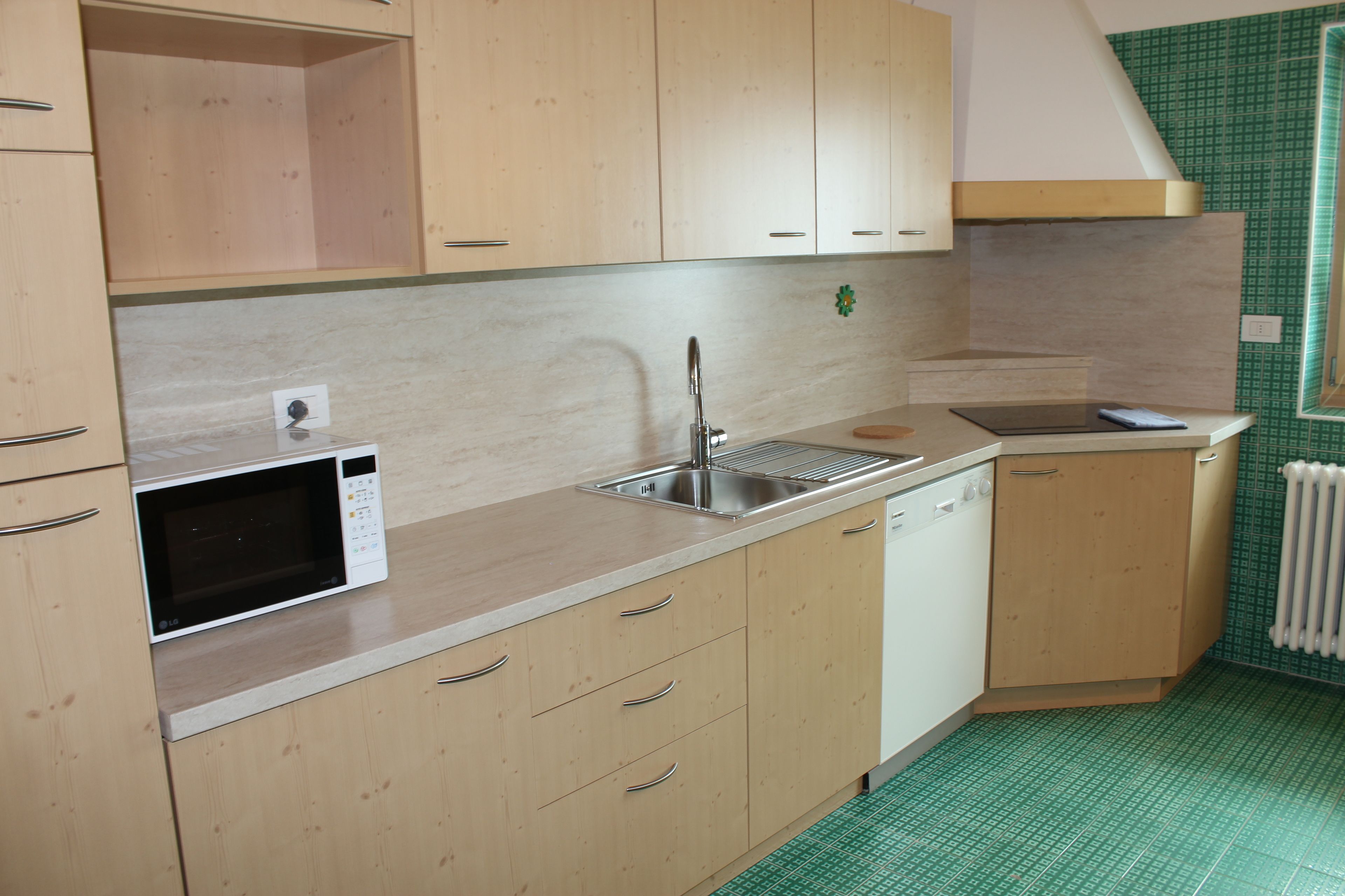 A kitchen with wooden cabinets, a microwave, a sink, and a window with a green patterned view.