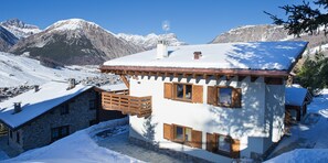 A snow-covered mountain house with wooden balconies and a stone exterior. - Chalet Elena (Livigno)