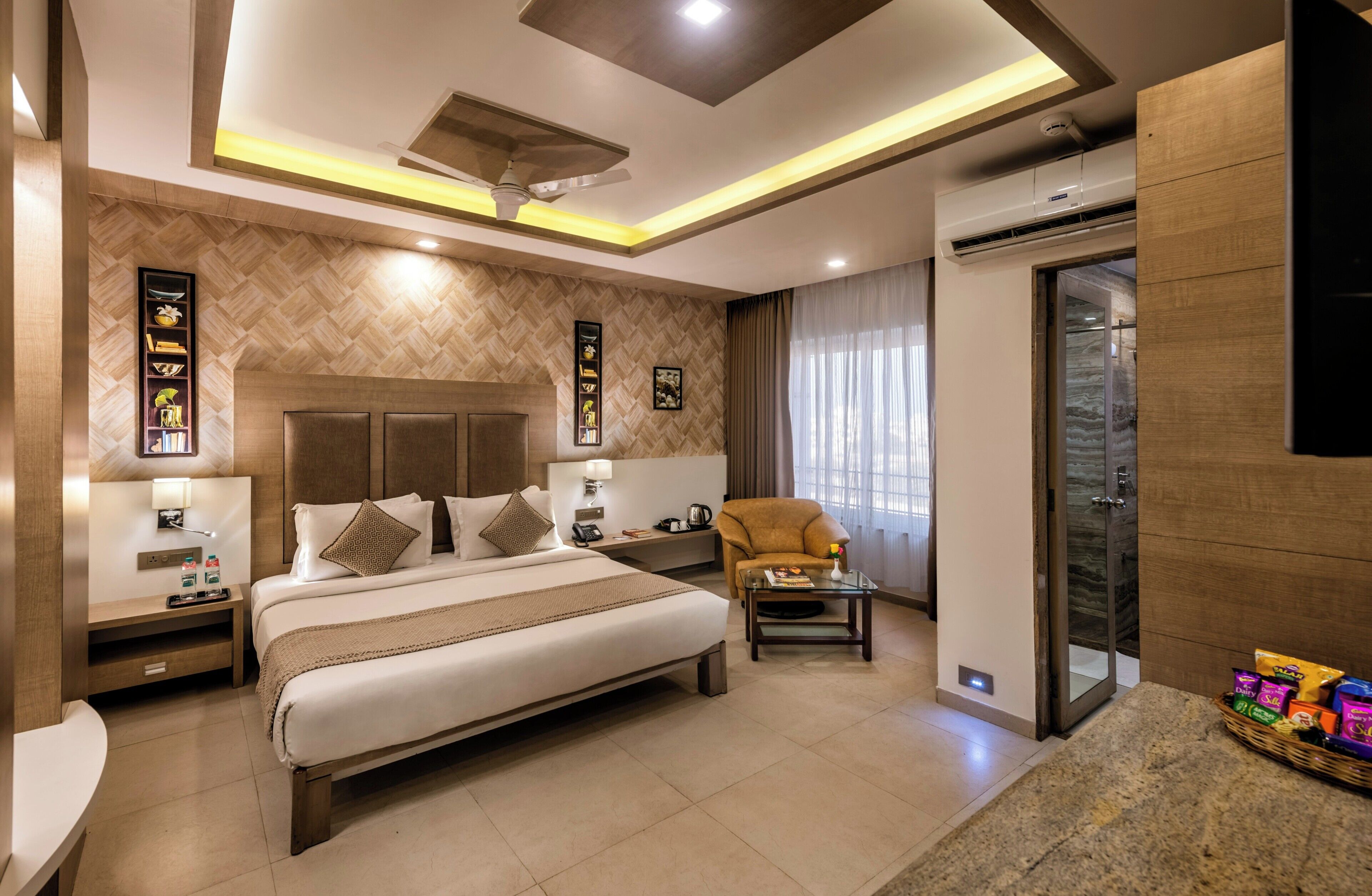 Una habitación de hotel moderna con una cama grande, una zona de estar, televisión y puerta de cristal que da a un balcón.