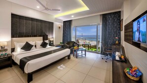 Ein modernes Hotelzimmer mit Bett, Schreibtisch, Fernseher, Balkon mit Aussicht und Deckenventilator.