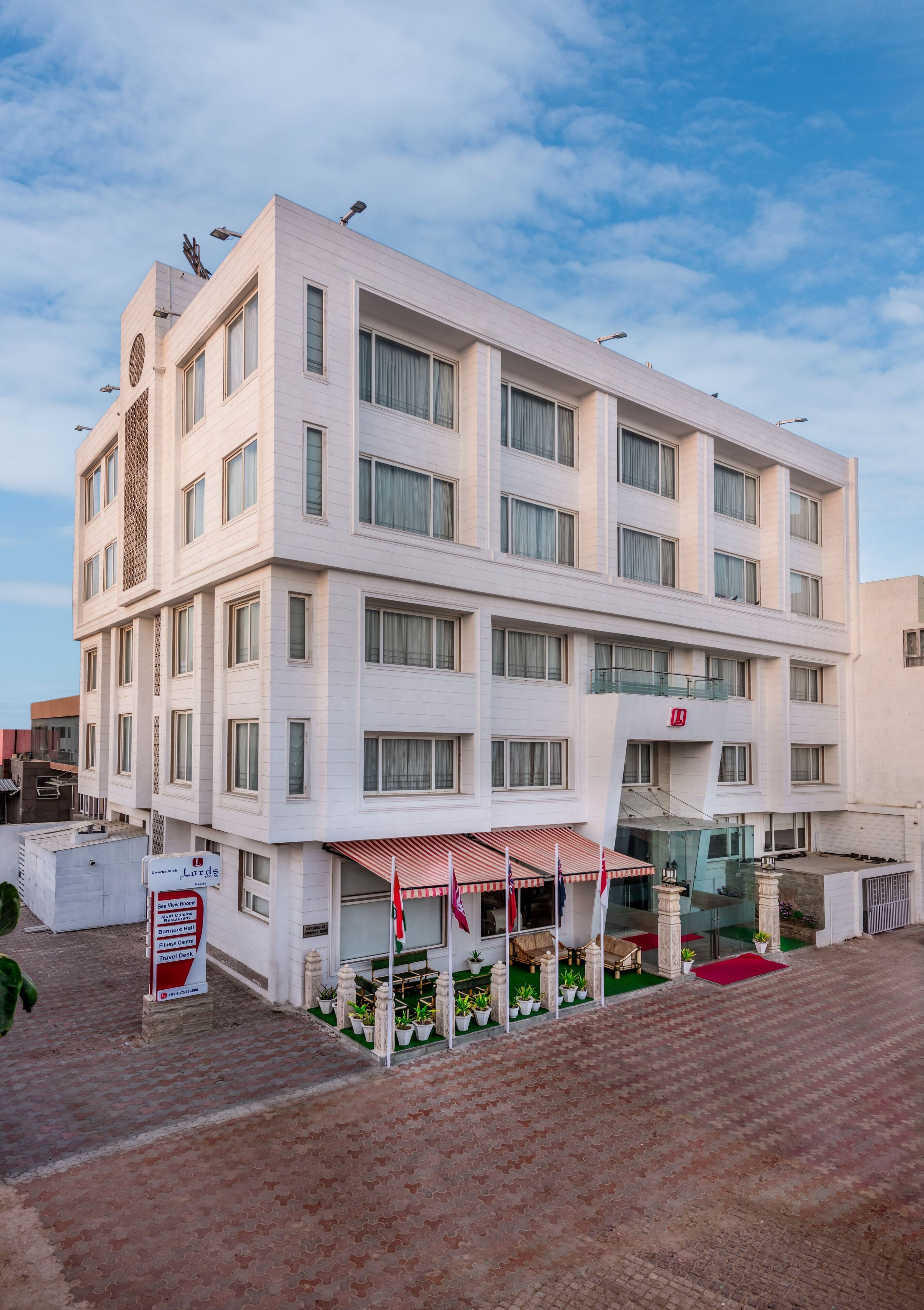 Un hotel de varios pisos con diseño moderno, que cuenta con una zona de estar exterior cubierta y plantas en macetas.