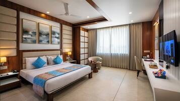 A hotel room with a large bed, bedside tables, a desk, a chair, a TV, and a ceiling fan.