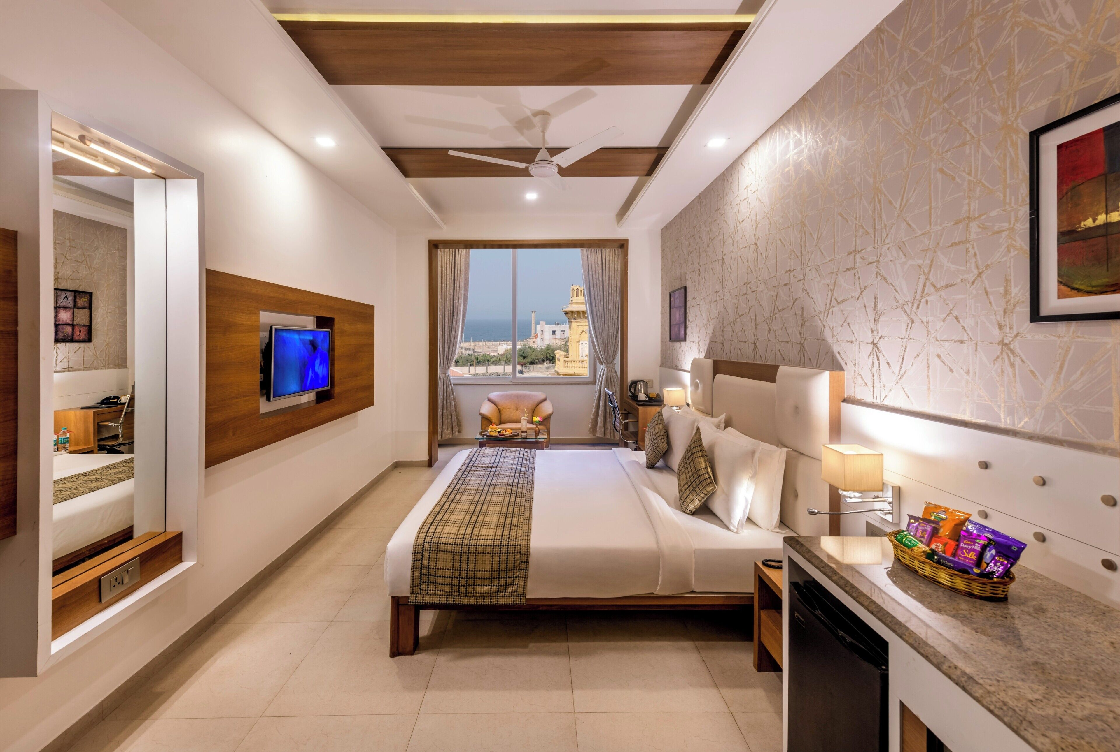 Ein Hotelzimmer mit einem großen Bett, einem Fernseher, einem Balkon mit Blick auf einen Turm und einer Minibar.