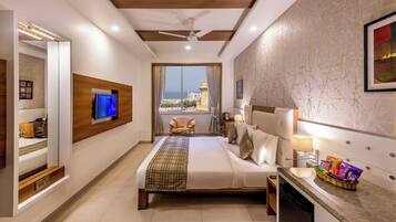 Ein Hotelzimmer mit einem großen Bett, einem Fernseher, einem Balkon mit Blick auf einen Turm und einer Minibar.