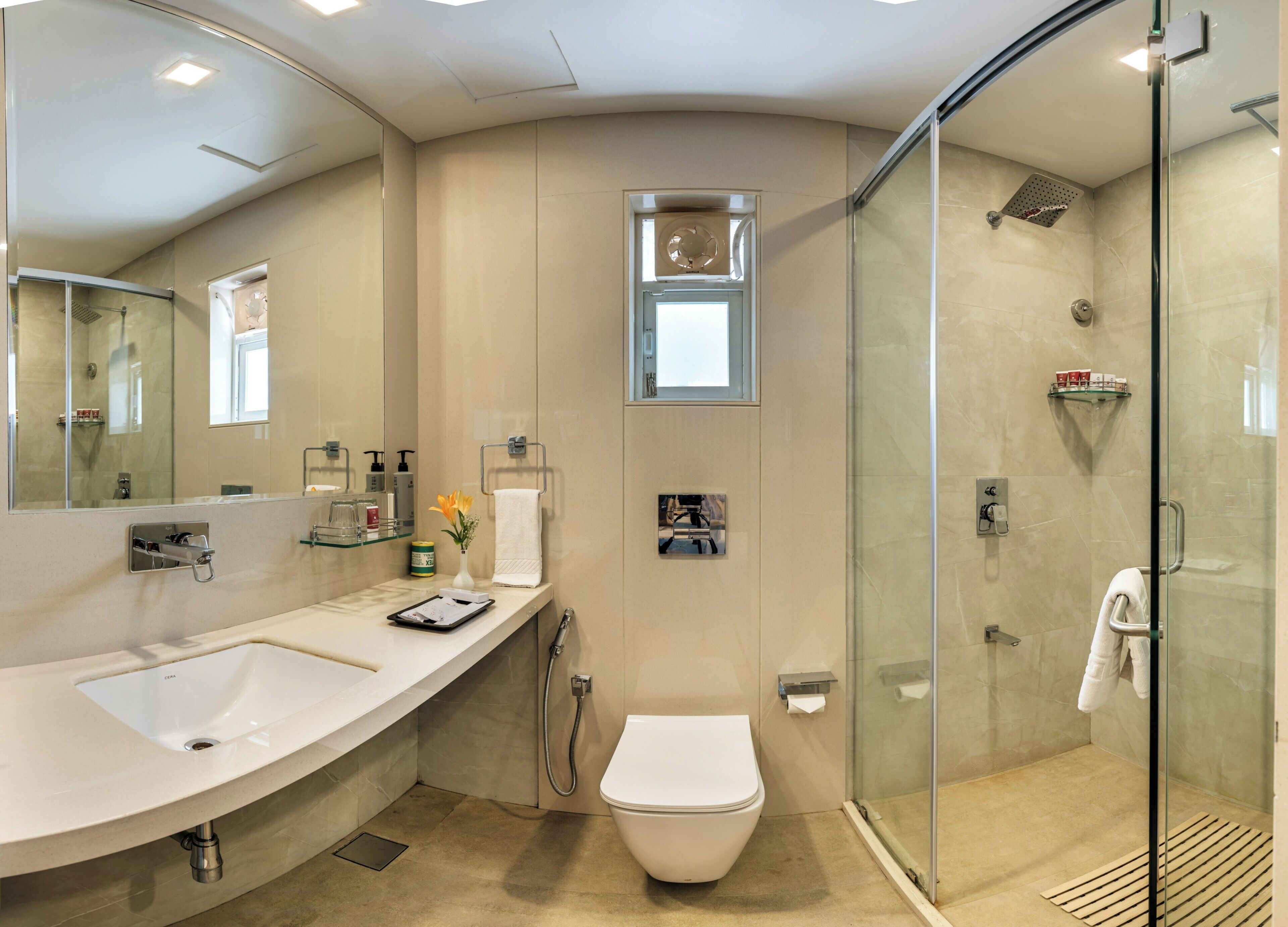 A modern bathroom with a curved sink, a toilet, a glass shower enclosure, and a small window.