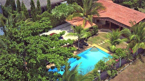 An aerial view of a resort with a swimming pool surrounded by lush greenery and palm trees.