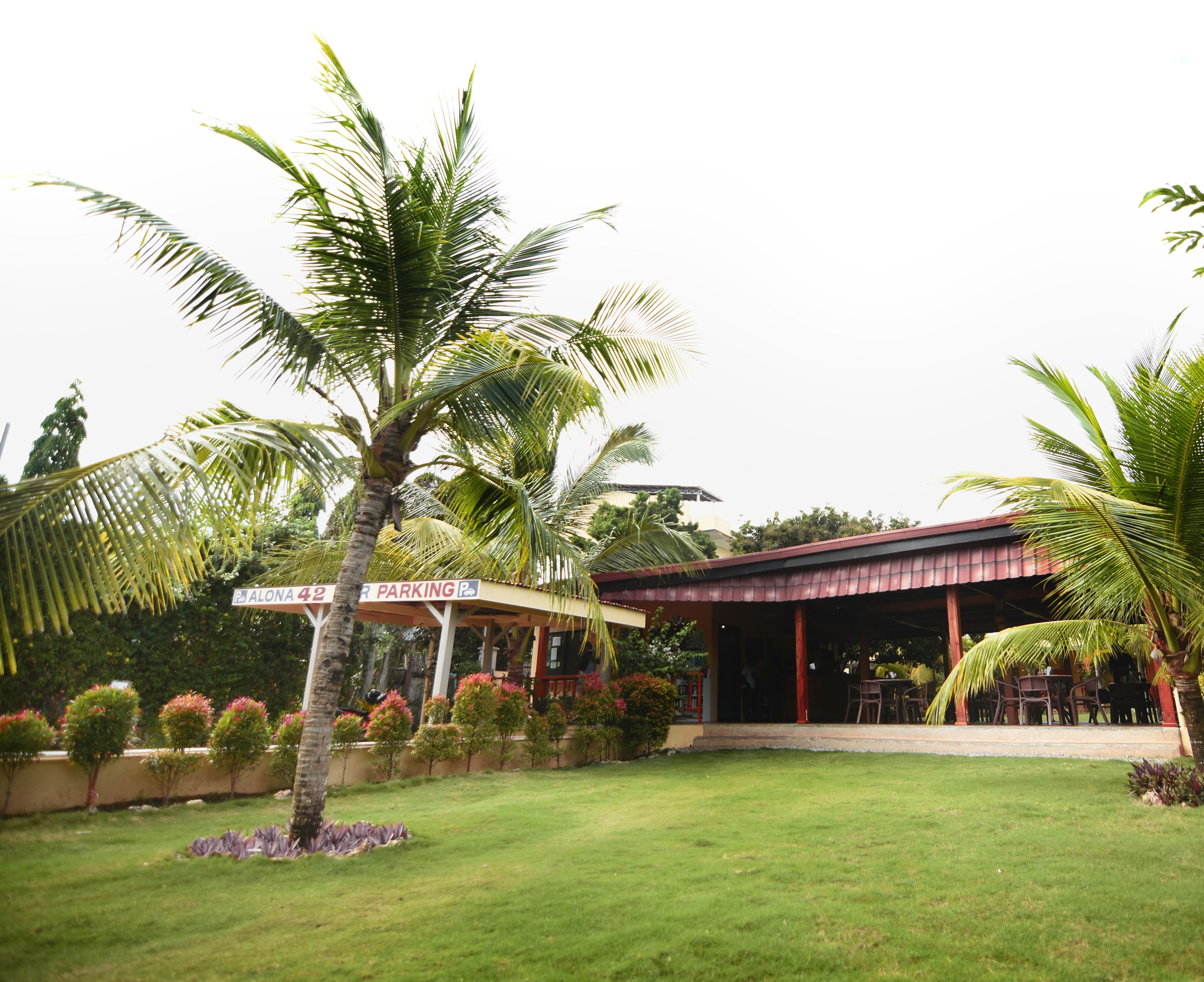 A building with a covered outdoor area, a sign indicating parking, and a well-maintained lawn.