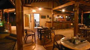 An outdoor wooden deck with tables and chairs, a bar area, and a view of the night sky.
