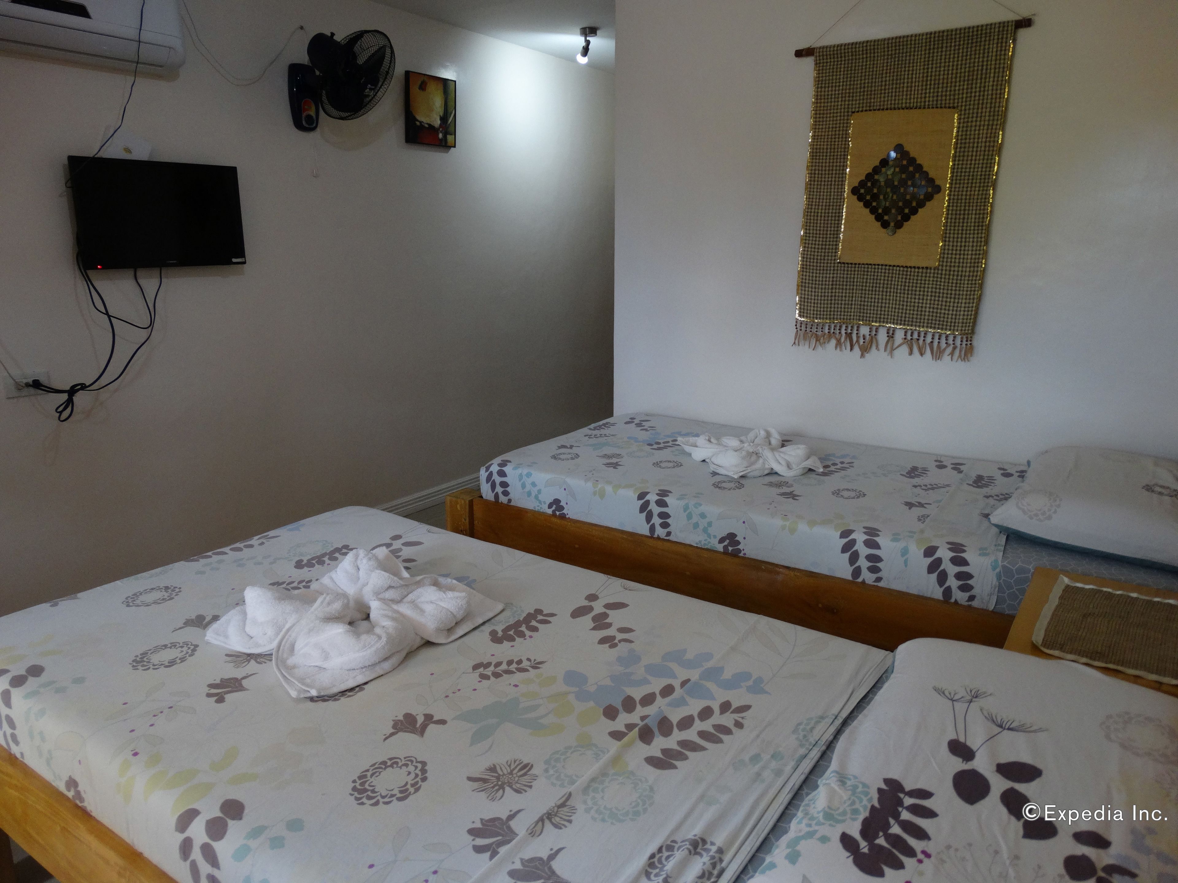 Un dormitorio con dos camas individuales, un televisor montado en la pared y un adorno colgando.