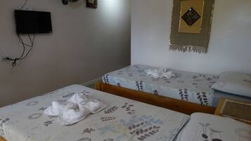 A bedroom with two single beds, a TV mounted on the wall, and a wall hanging.