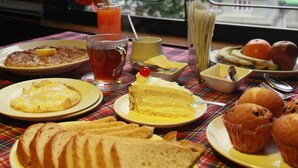 A breakfast table with various food items and a view of trees and buildings through a window.