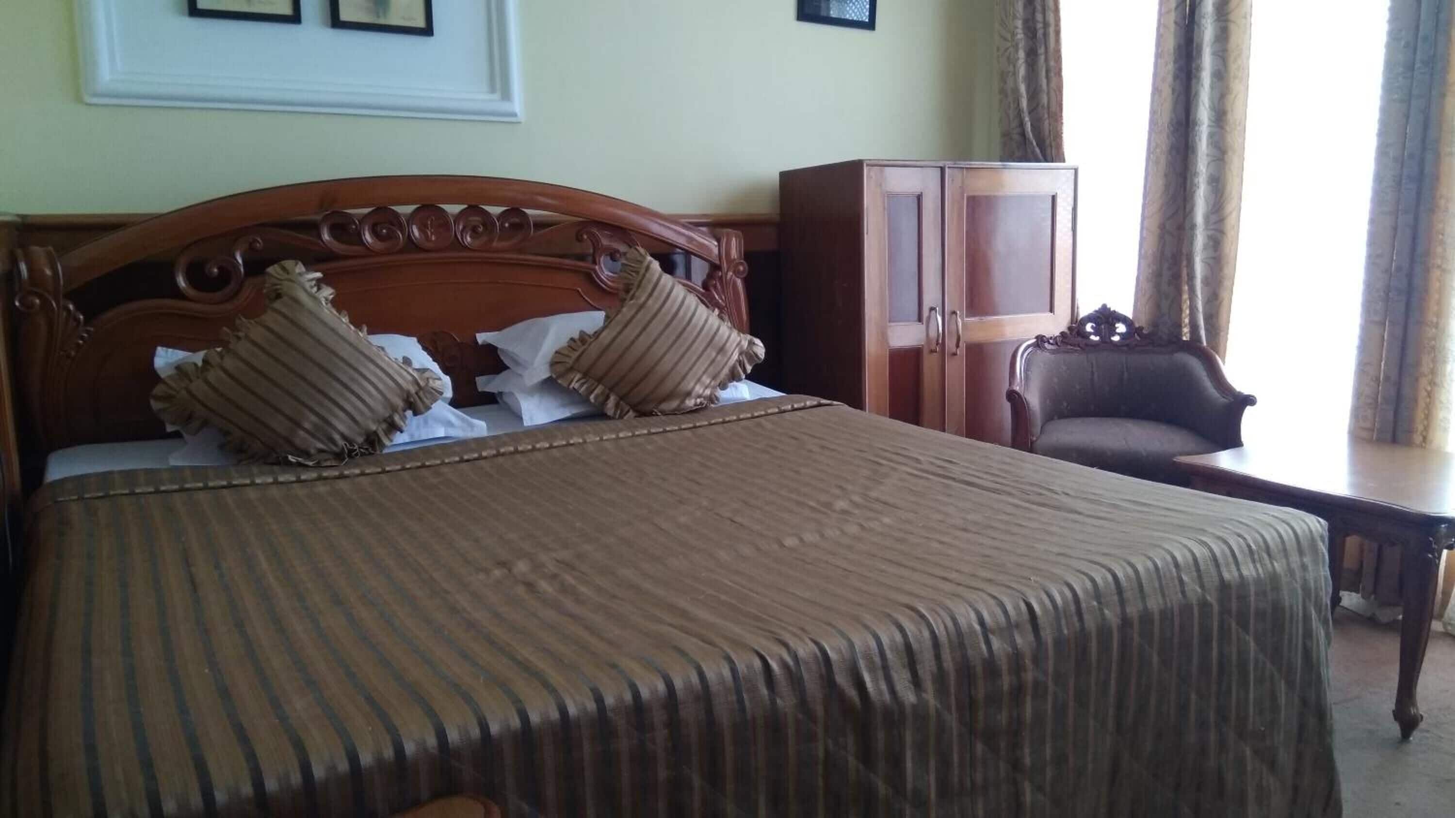 Un lit bien fait, recouvert d’une couvre-lit à rayures et agrémenté de deux oreillers, une armoire en bois et une chaise dans une pièce aux murs de couleur claire et dotée d’une fenêtre avec des rideaux.