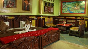 A traditional room with a large bed, a small table, and a chair. There are paintings on the walls and a large mural.