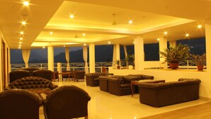 A spacious lounge area with multiple seating options, large windows offering views of the outdoors, and a balcony with a railing. - Saramsa Resort (Gangtok)