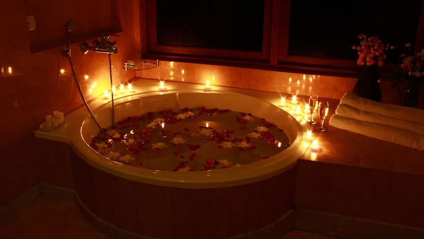 A dimly lit room with a bathtub filled with water and rose petals, surrounded by candles, and a window with a view of the night sky. - Saramsa Resort (Gangtok)