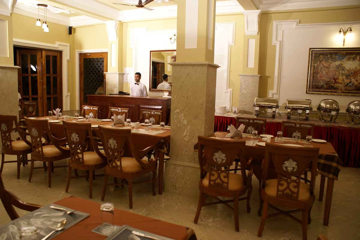 Un comedor con mesas y sillas de madera, un pilar de mármol y una barra tipo buffet.